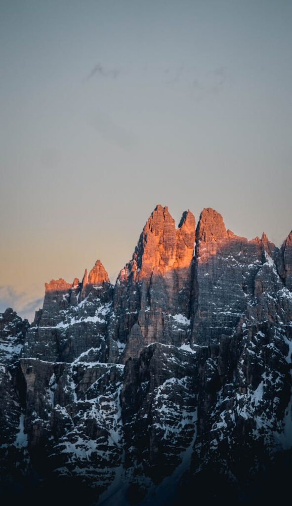 A breathtaking view of snowy mountain peaks in the Dolomites during sunset, with a warm glow.